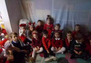 Grupka dzieci siedzi na podłodze czekając na Mikołaja.