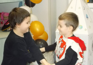 Dwóch chłopców trzyma się za ręce w zabawie. Uśmiechają się do siebie.