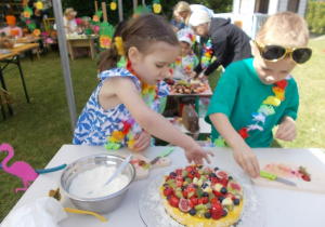 Zosia i Kacper, reprezentacji naszego przedszkola, układają różne owoce na serniczku z mango.