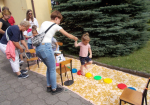 Dziewczynka przechodzi po sensorycznym, wypukłym torze. Jedną ręką asekuruje ją mama.