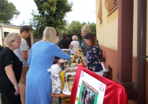 Rodzice zebrani przy stole z kawą, herbatą, surówkami i innymi dodatkami w oczekiwaniu na kiełbaskę i kaszankę z grilla.