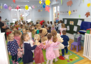 Dzieci ustawione w rzędach, tworzą "pociągi". W jednej z dłoni trzymają przyniesione z domu misie i inne pluszaki.