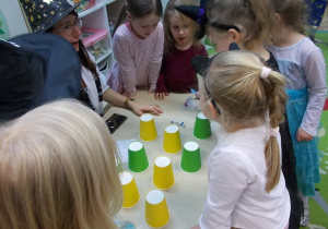Dzieci stoją dookołą stolika na któym ułożone są żółte i zielone kubeczki. Podnoszą wybrany, a jedna z pań czyta wróżbę.
