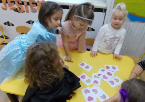 Dziewczynki stoją przy stoliku, na któym rozłożóne są karty. Losują kolejno po jednej.