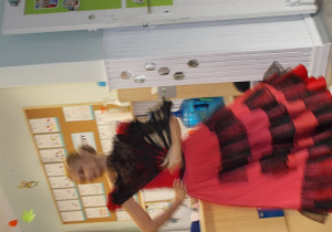 Pani w czerwono-czarnej sukience z falbanami. W ręce trzyma rozłożony czarny wachlarz.