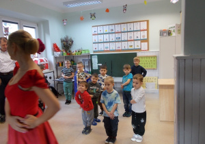 Kilkoro chłopców naśladuje ruchy jednej z tancerek - trzymają dłonie w pasie.