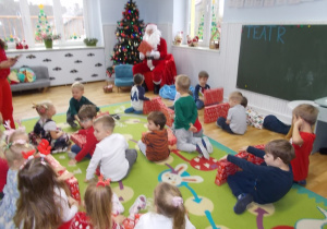 Mikołaj siedzi, rozdaje dzieciom prezenty.