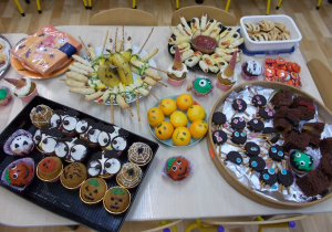 Na stole rozłożone różne przekąski: mumie z ciasta francuskiego, mandarynkowe stworki, pajączki z ciastek oreo.