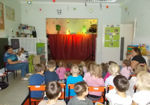 Dzieci siedzą na krzesłąch. Przed nimi ustawiona scena.