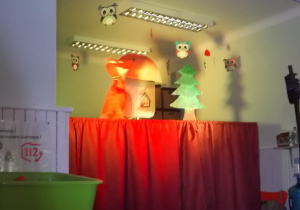 Na scenie, wysoko kukiełka lisa i choinki.