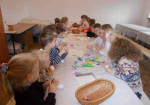 Dzieci trzymają białe jajko. Na stole rozłożone kolorowe pisaki. Dzieci rysują wzory na swoich jajkach.