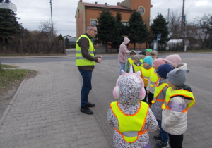 Grupa dzieci stoi na chodniku. Wita ją pracownik ZEC ubrany w kamizelkę odblaskową.