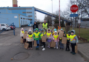 Dzieci trzymając papierowe torby, w których są upominki, pozują do wspólnego zdjęcia przed bramą główną.p