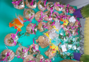 Babeczki owinięte różową wstążką oraz ciasteczka z żółtą wstążką. Między nimi ustawione kurczaczki wykonane z tektury.