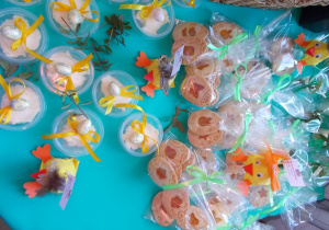 Ciasteczka udekorowane zieloną wstążką oraz pojemniczki z masełkiem przystrojone borówkami i żółtą kokardą.