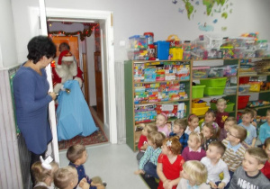Pani nauczycielka otwiera drzwi od sali. W nich stoi Święty Mikołaj. W jednej ręce trzyma przed sobą ogromny niebieski worek, w drugiej macha dzwoneczkiem.