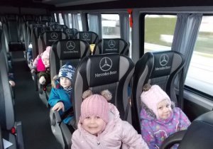 Wnętrze busa. Dzieci siędzą kolejno po dwoje. Uśmiechają się.