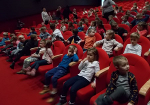 Widownia w teatrze. Dzieci siedzą w rzędach na czerwonych fotelach czekając na przedstawienie.