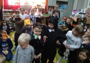 Dzieci w maskach kotków stoją po środku dywanu i pokazują swoje stroje.