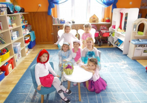 Wszystkie dziewczynki pozują do zdjęcia. Czerwony Kapturek siedzi na krześle, Kotek kuca przy stoliku, na kanapie siedzi Elza, Masza i Kopciuszek za nimi stoją Aniołek i Dzwoneczek.