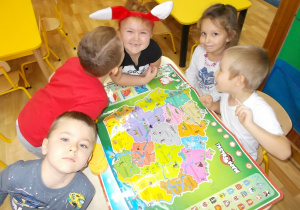 Piątka dzieci siedzi przed rozłożoną matą dydaktyczną o Polsce.